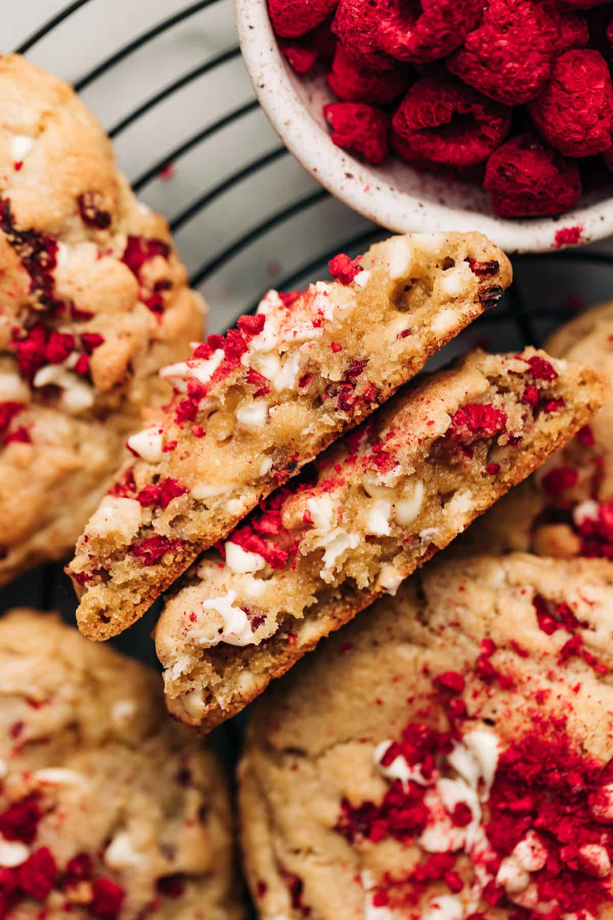 Raspberry white chocolate chip cookies cut in half on a black wire rack.