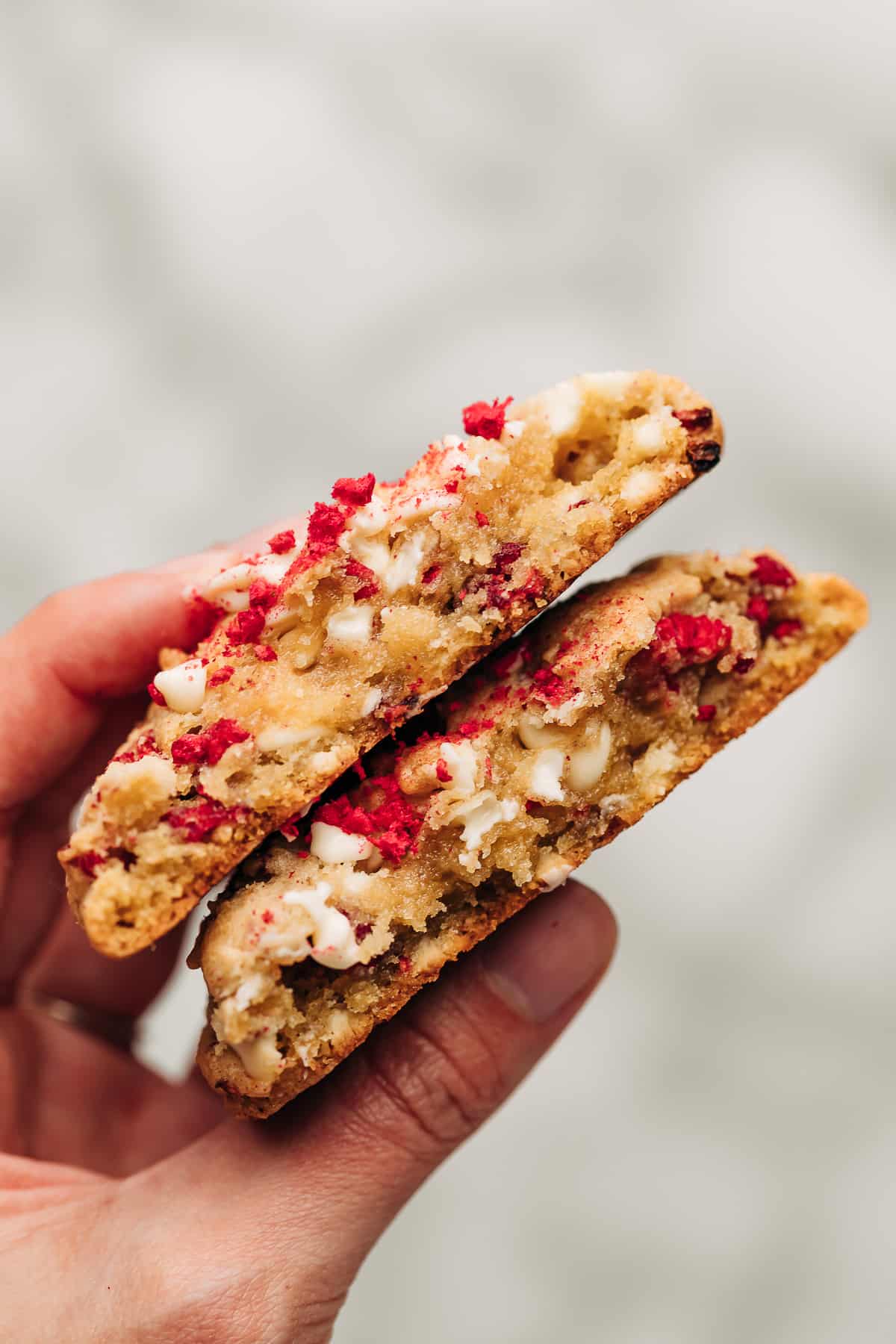 Hand holding stack of raspberry white chocolate chip cookies cut in half.