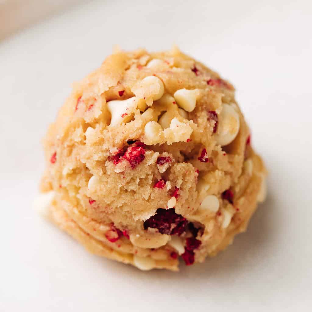 Unbaked raspberry white chocolate chip cookie on parchment paper.