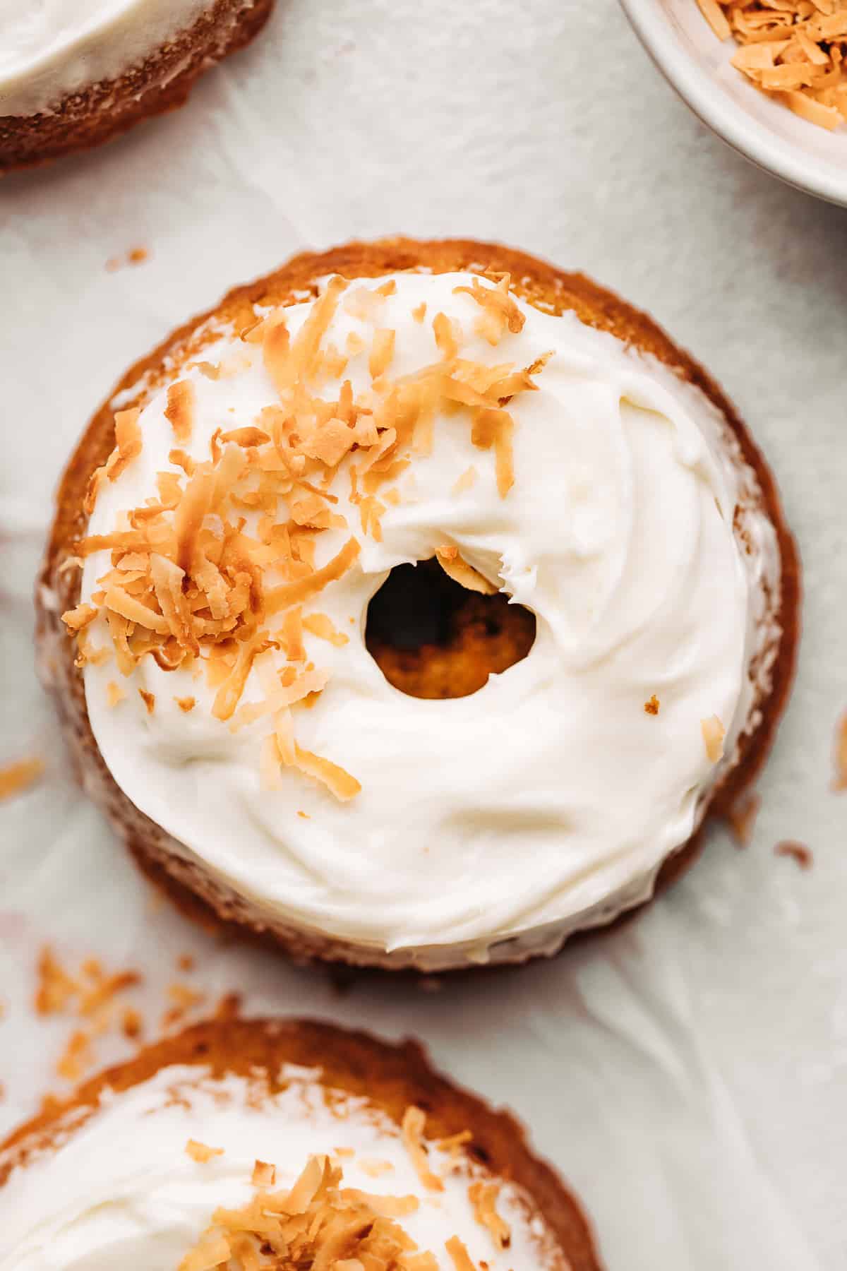 carrot cake donut with cream cheese frosting and toasted coconut flakes on parchment paper.