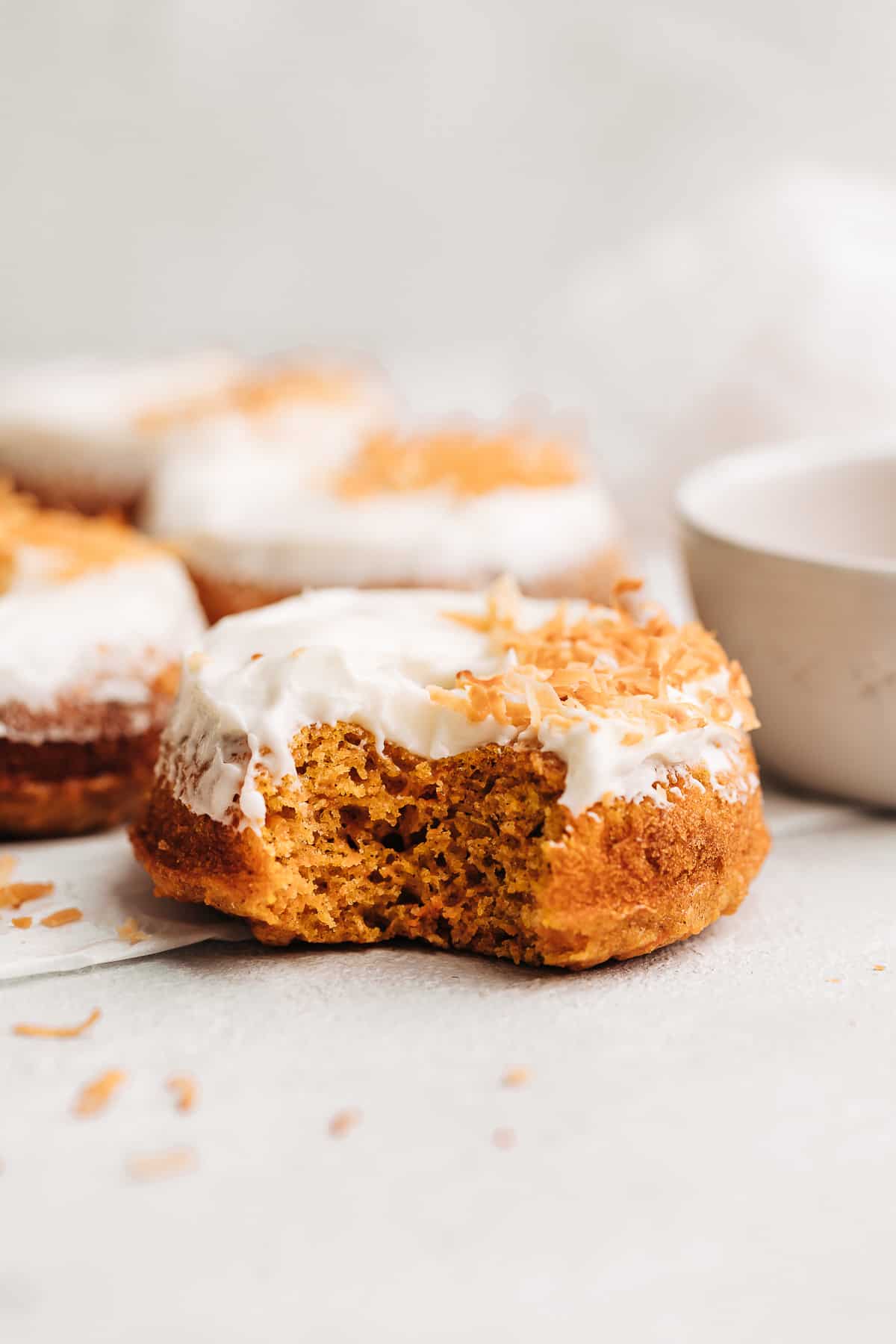 Bite shot of a carrot cake donut with cream cheese frosting and toasted coconut flakes.