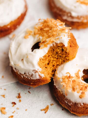 Bite shot of a carrot cake donuts with cream cheese frosting and toasted coconut.