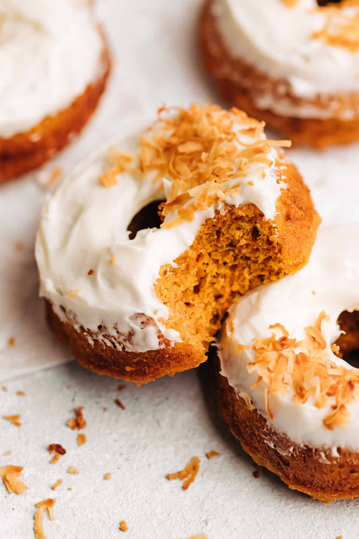 Bite shot of a carrot cake donuts with cream cheese frosting and toasted coconut.