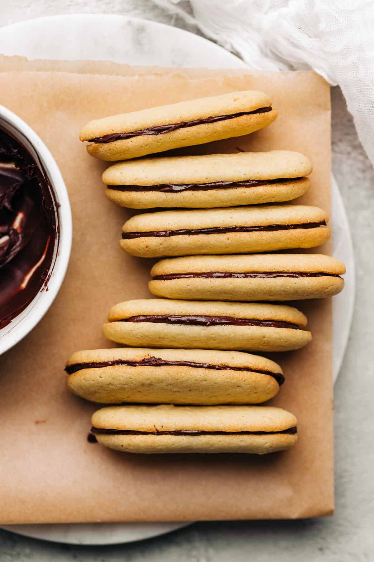 Milano cookies and bowl of ganache on brown parchment paper.a