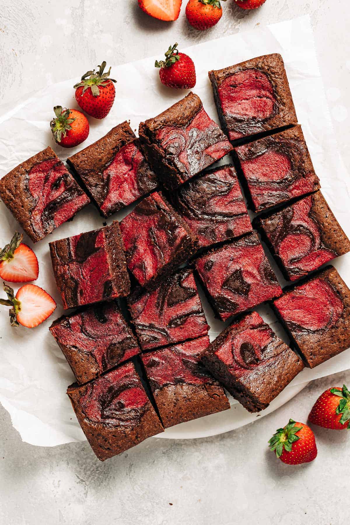 strawberry swirl brownies on parchment paper with fresh starwberries.