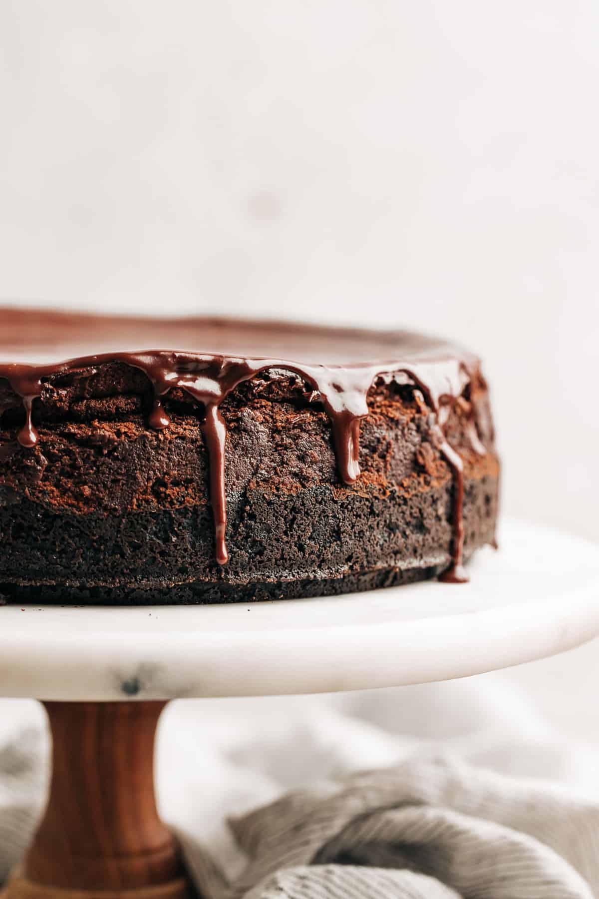 chocolate cheesecake with ganache on a marble cake stand.