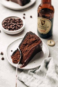 slice of chocolate cheesecake on a plate and a bowl of chocolate chips and bottle of stout.