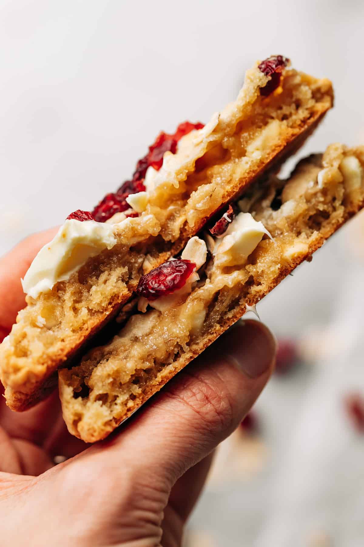 hand holding a white chocolate cranberry oatmeal cookie cut in half.
