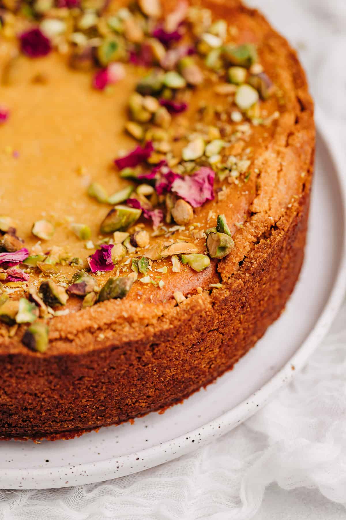 close up picture of a Persian love cake on a white plate topped with pistachio and dried rose petals.