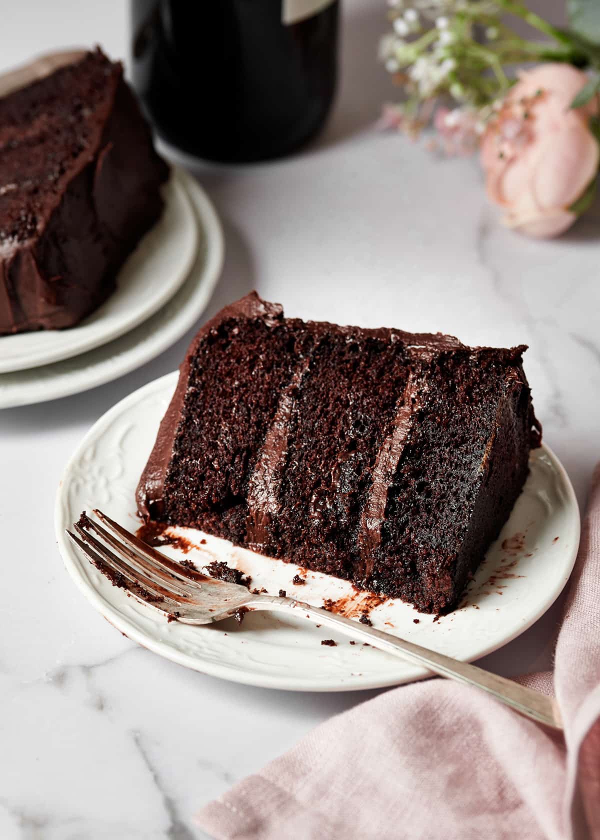a slice of red wine chocolate cake with chocolate cream cheese frosting on a plate.