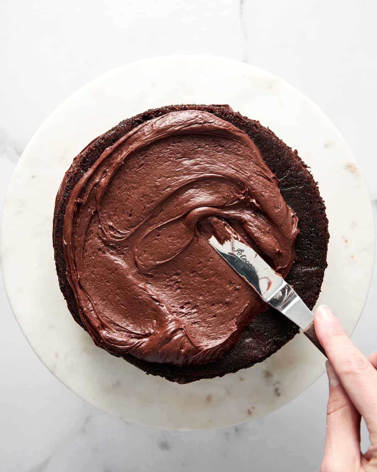 chocolate cream cheese frosting being spread onto a red wine chocolate cake.