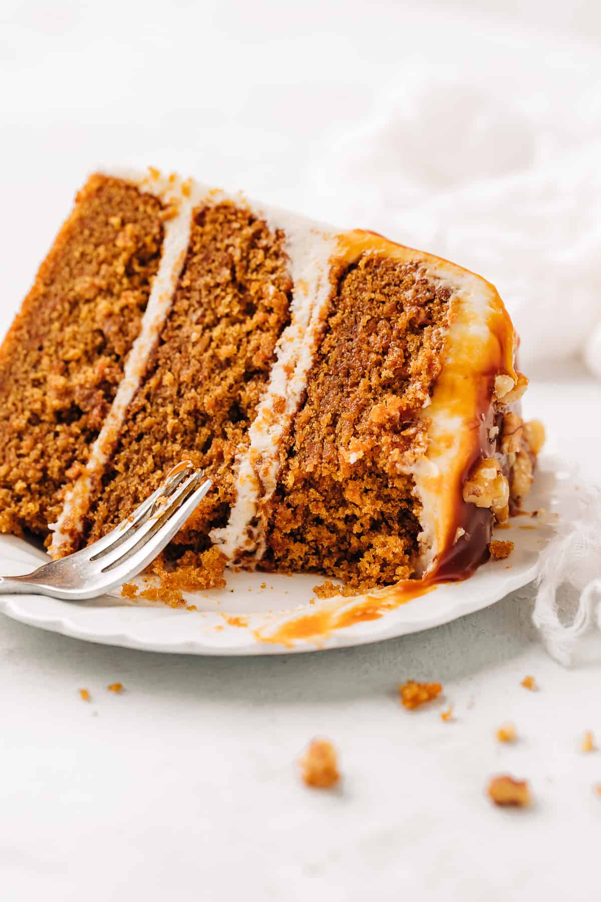 Slice of carrot cake with cream cheese frosting on a white plate.