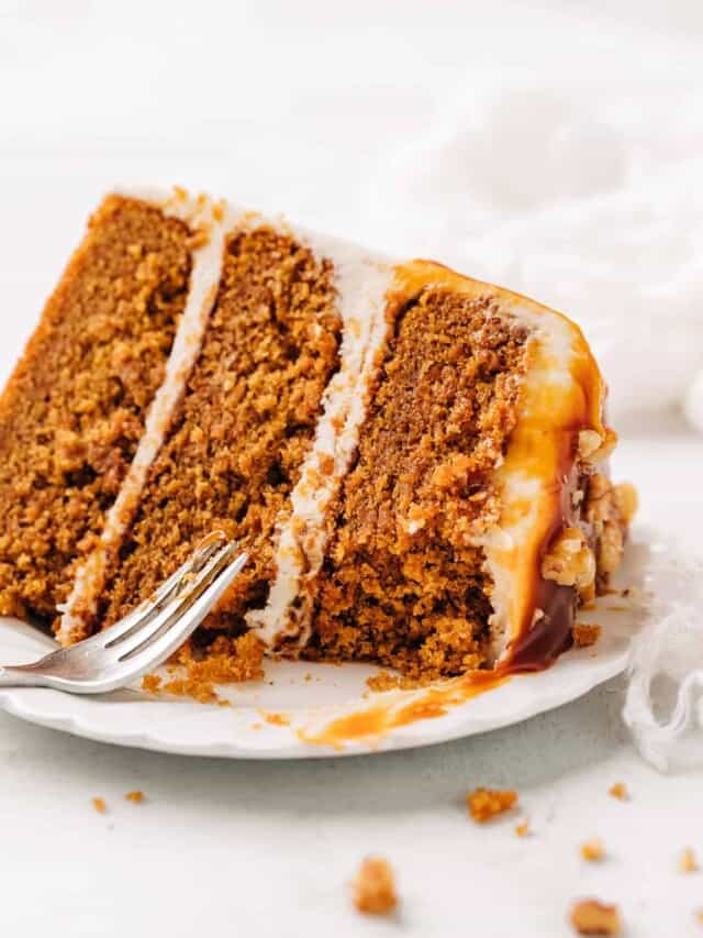 Slice of carrot cake with cream cheese frosting on a white plate.