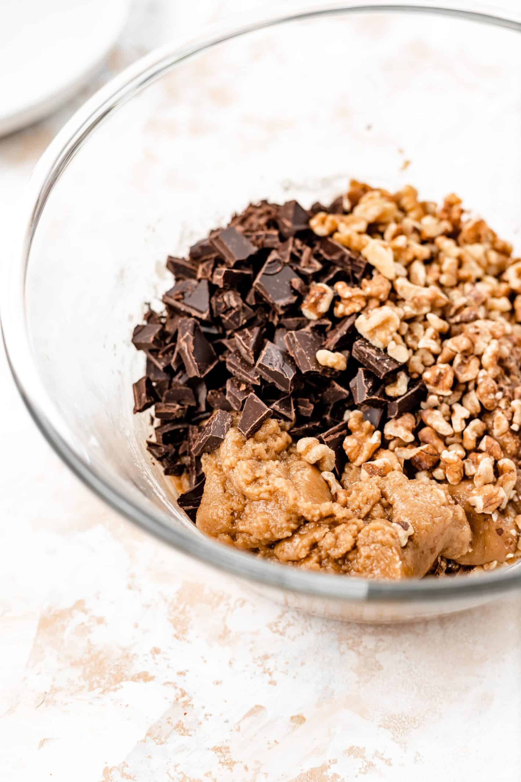 chopped chocolate, walnuts, and vegan cookie dough in a mixing bowl