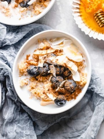 bulgur breakfast bowl topped with coconut flakes, blueberries, cinnamon, and honey