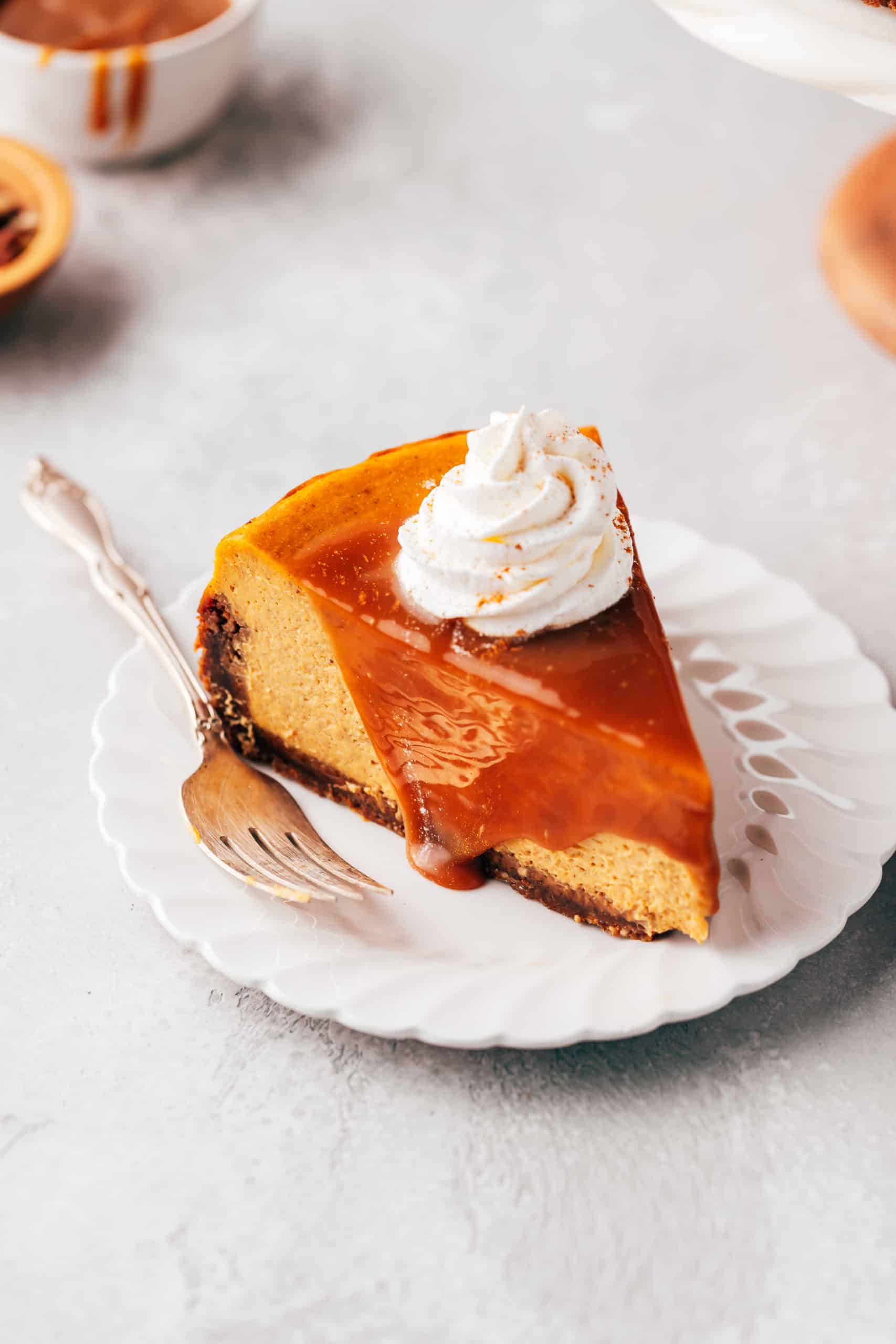 slice of pumpkin cheesecake with caramel sauce and whipped cream on a plate