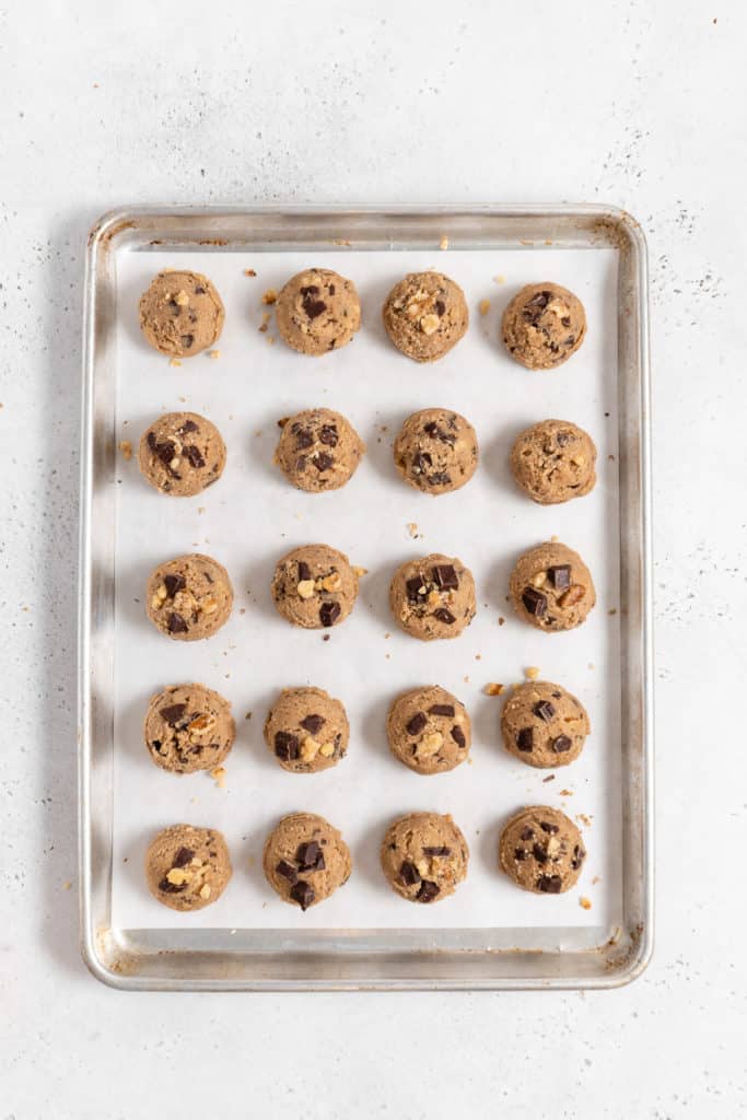 unbaked chocolate chip cookie dough balls on a parchment paper lined baking sheet