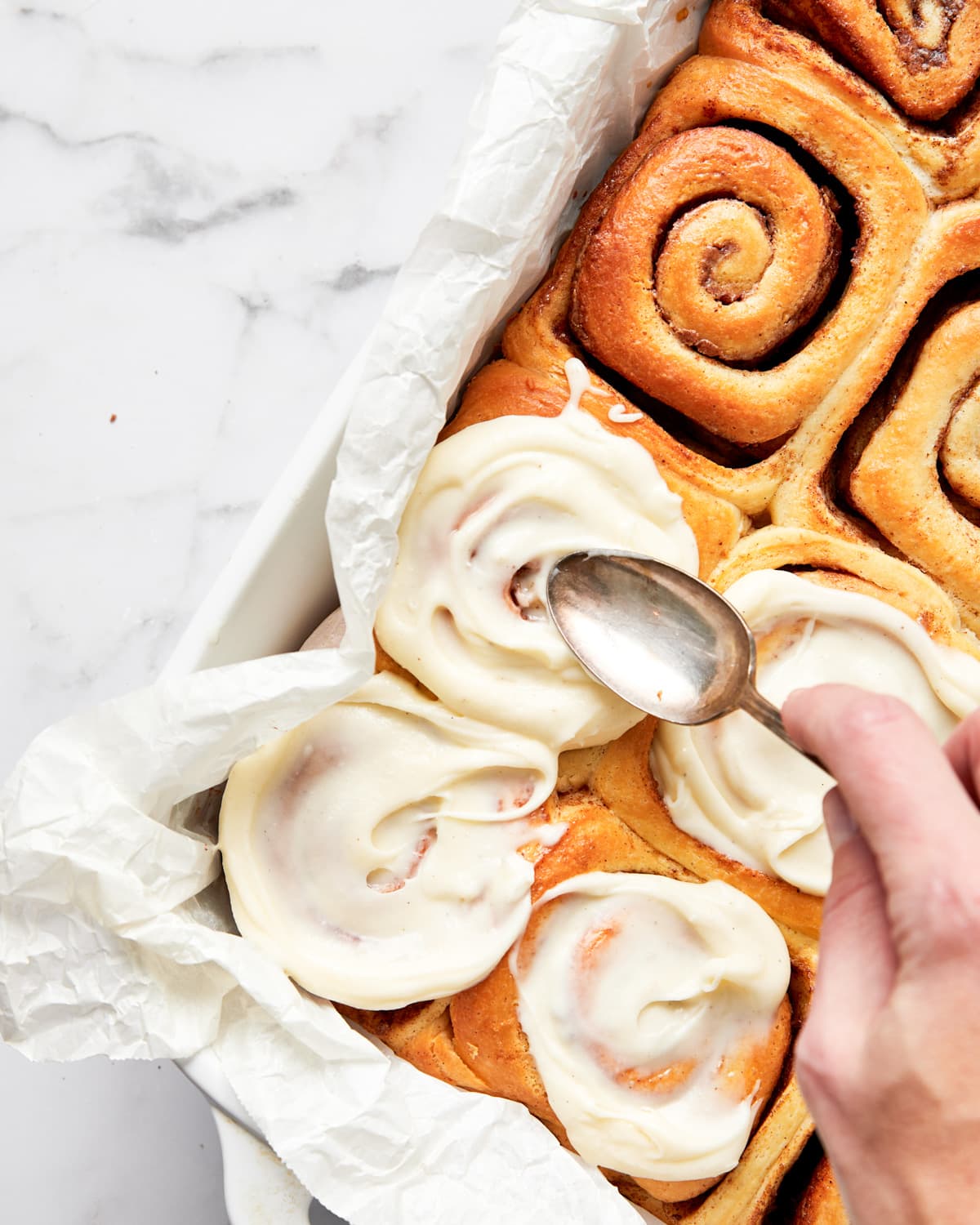 cream cheese icing being spread over warm cinnamon rolls.