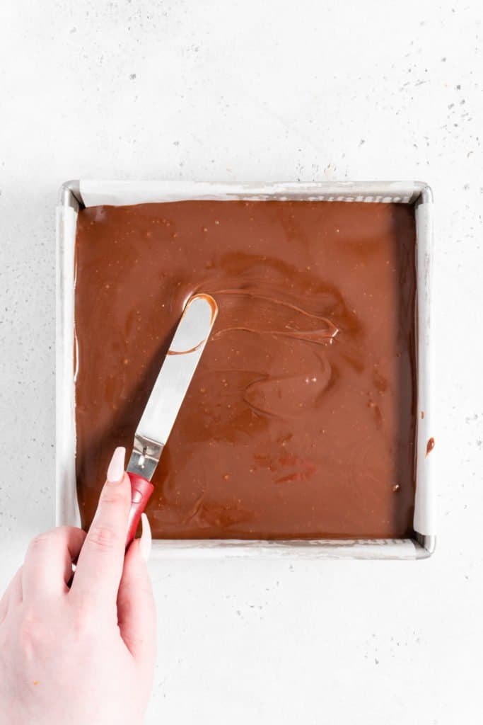 caramel ganache being spread on brownies