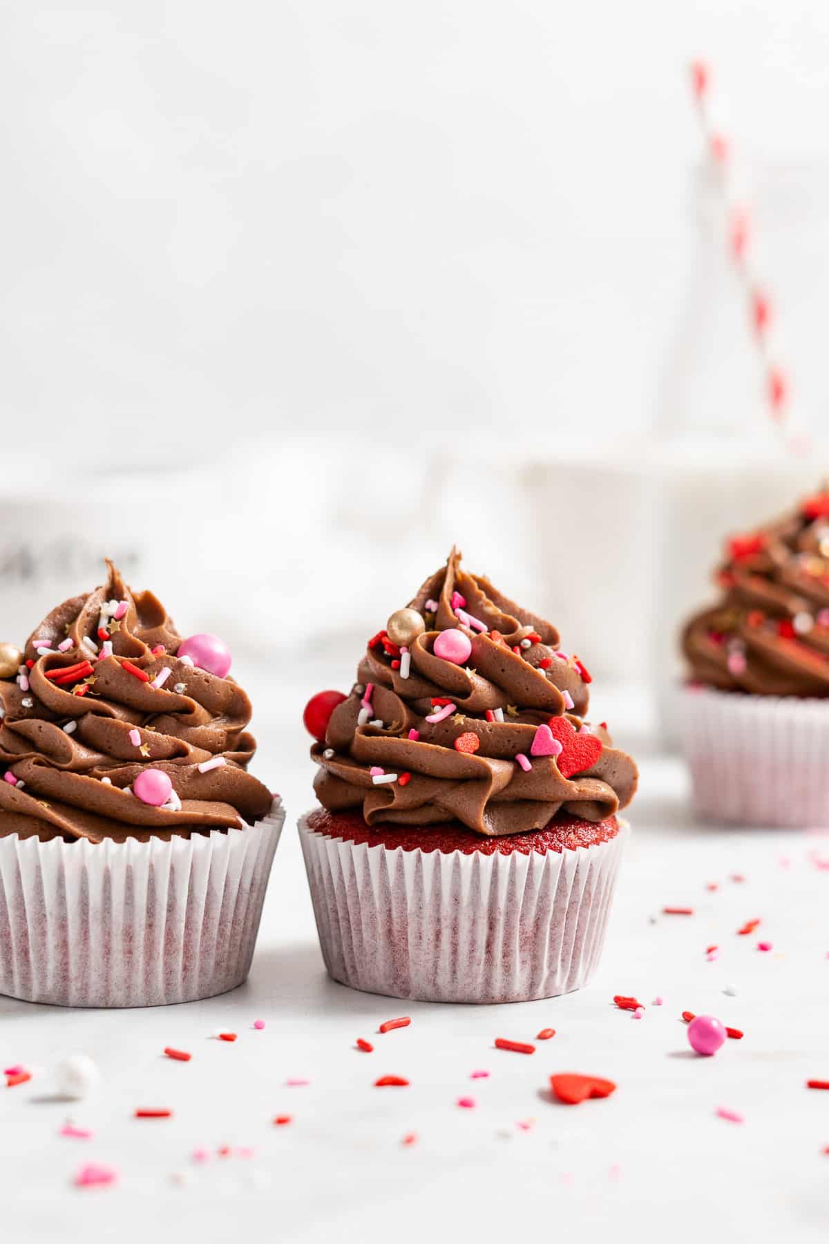 Three red velvet cupcakes with chocolate frosting and Valentine's Day sprinkles.