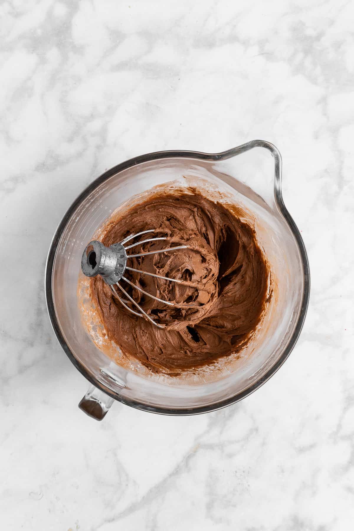chocolate cream cheese frosting in a glass mixing bowl with a whisk.