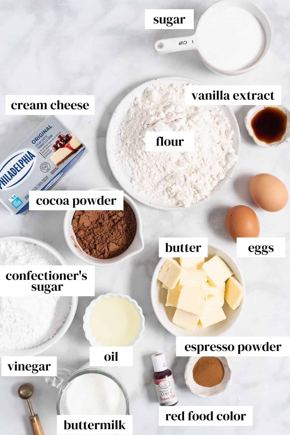sugar, flour, vanilla extract, eggs, butter, cream cheese, cocoa powder, confectioner's sugar, oil, red food coloring, and espresso powder on a marble countertop.