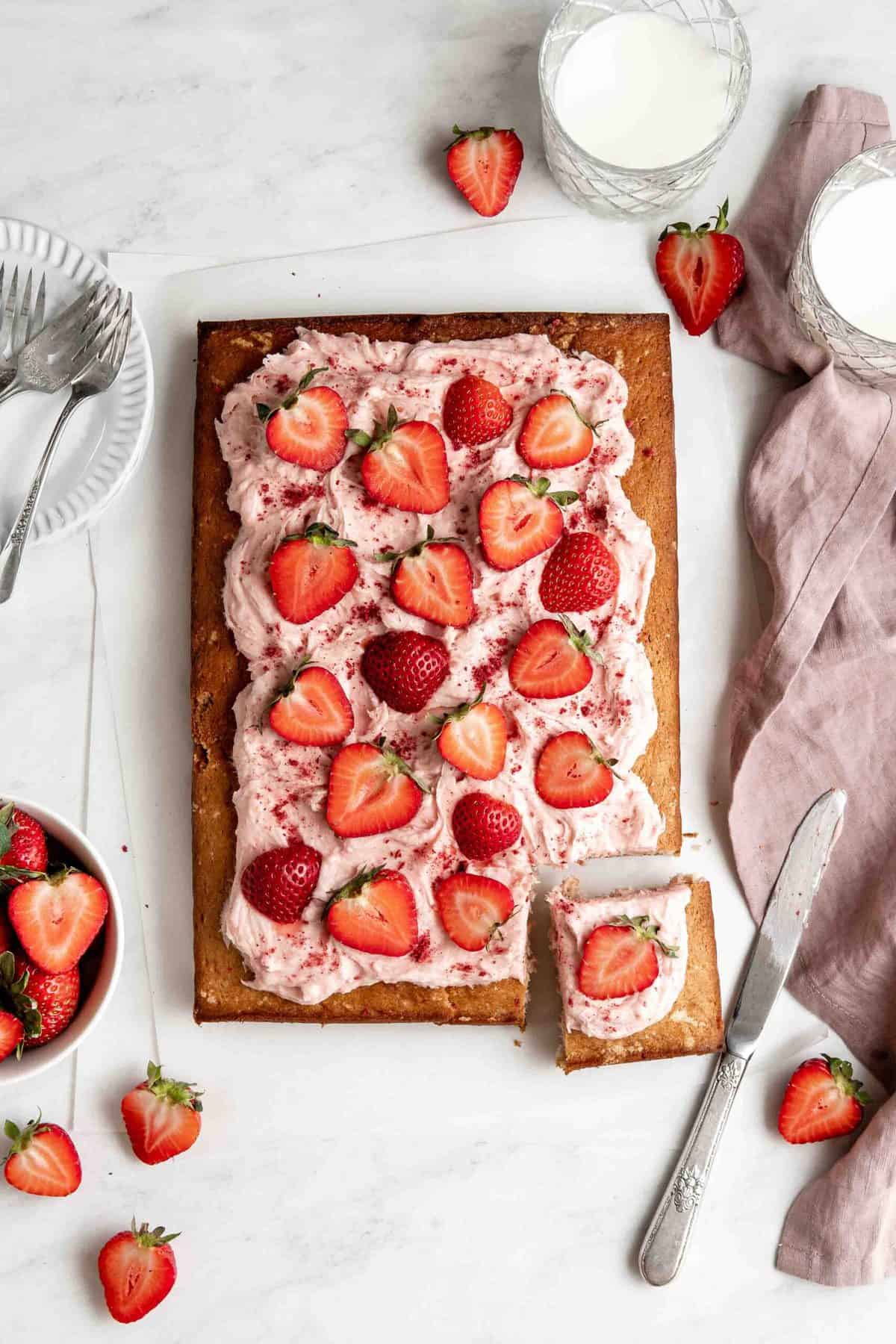 Strawberry sheet cake with strawberry cream cheese frosting topped with sliced strawberries.