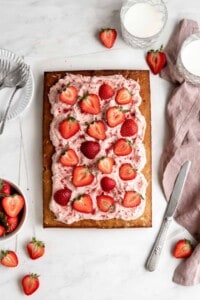 Strawberry sheet cake with strawberry cream cheese frosting topped with sliced strawberries.