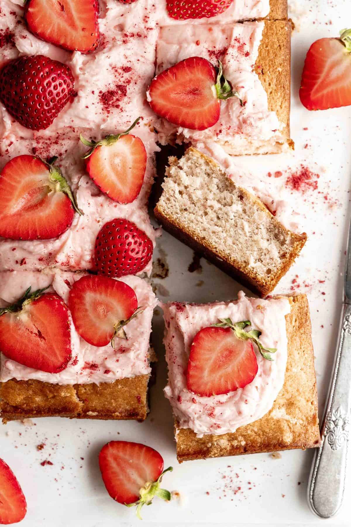 Slice of strawberry sheet cake with strawberry cream cheese frosting topped with sliced strawberries.