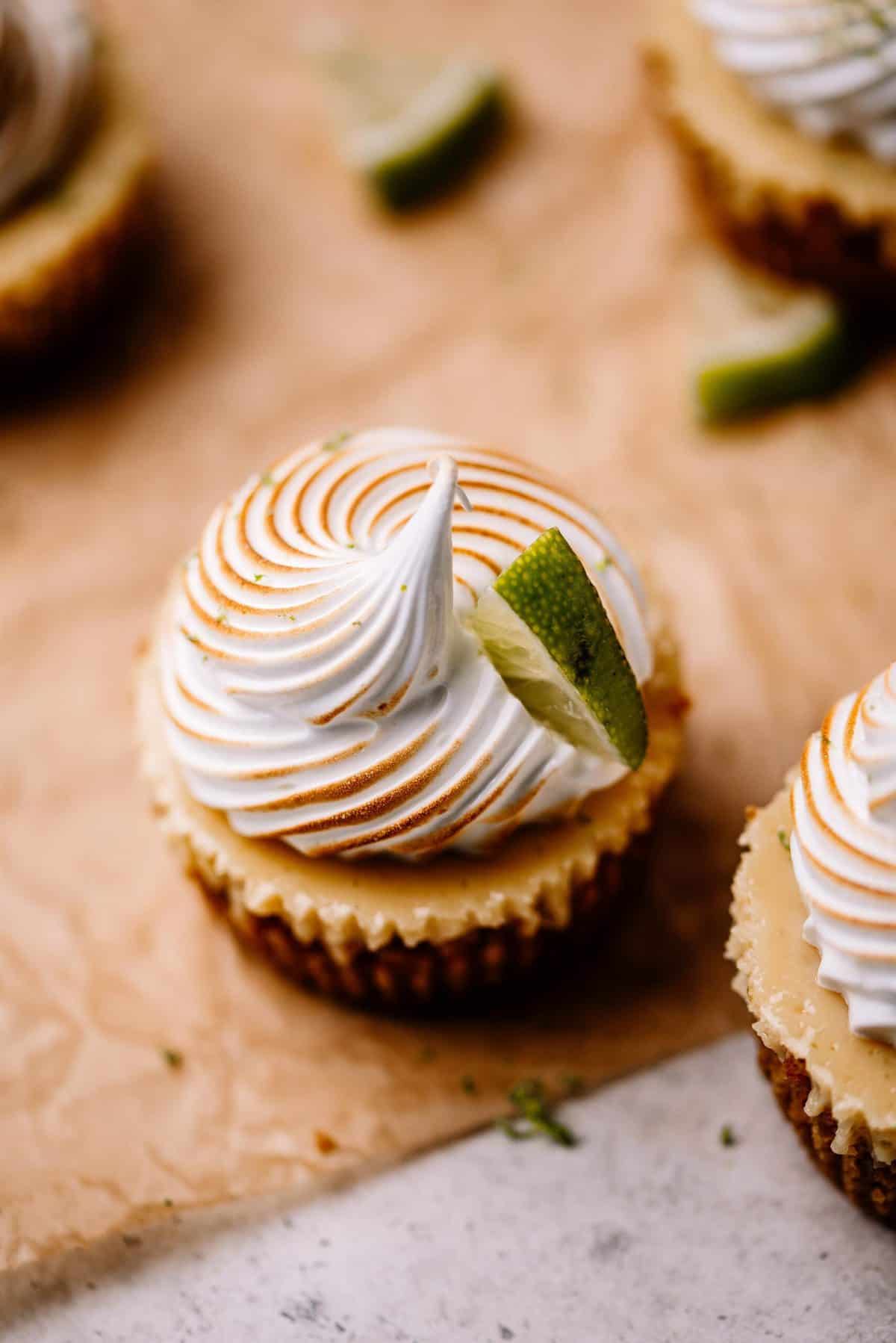 Mini key lime pie with meringue and a slice of lime on brown parchment paper.