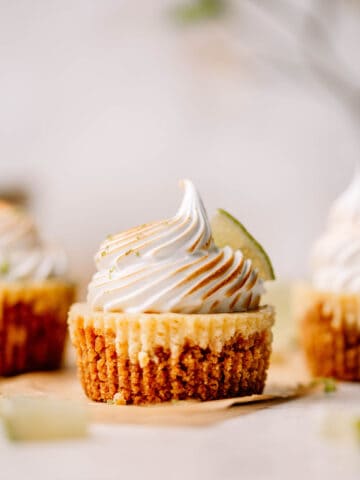 Mini key lime pie with meringue and a slice of lime on brown parchment paper.