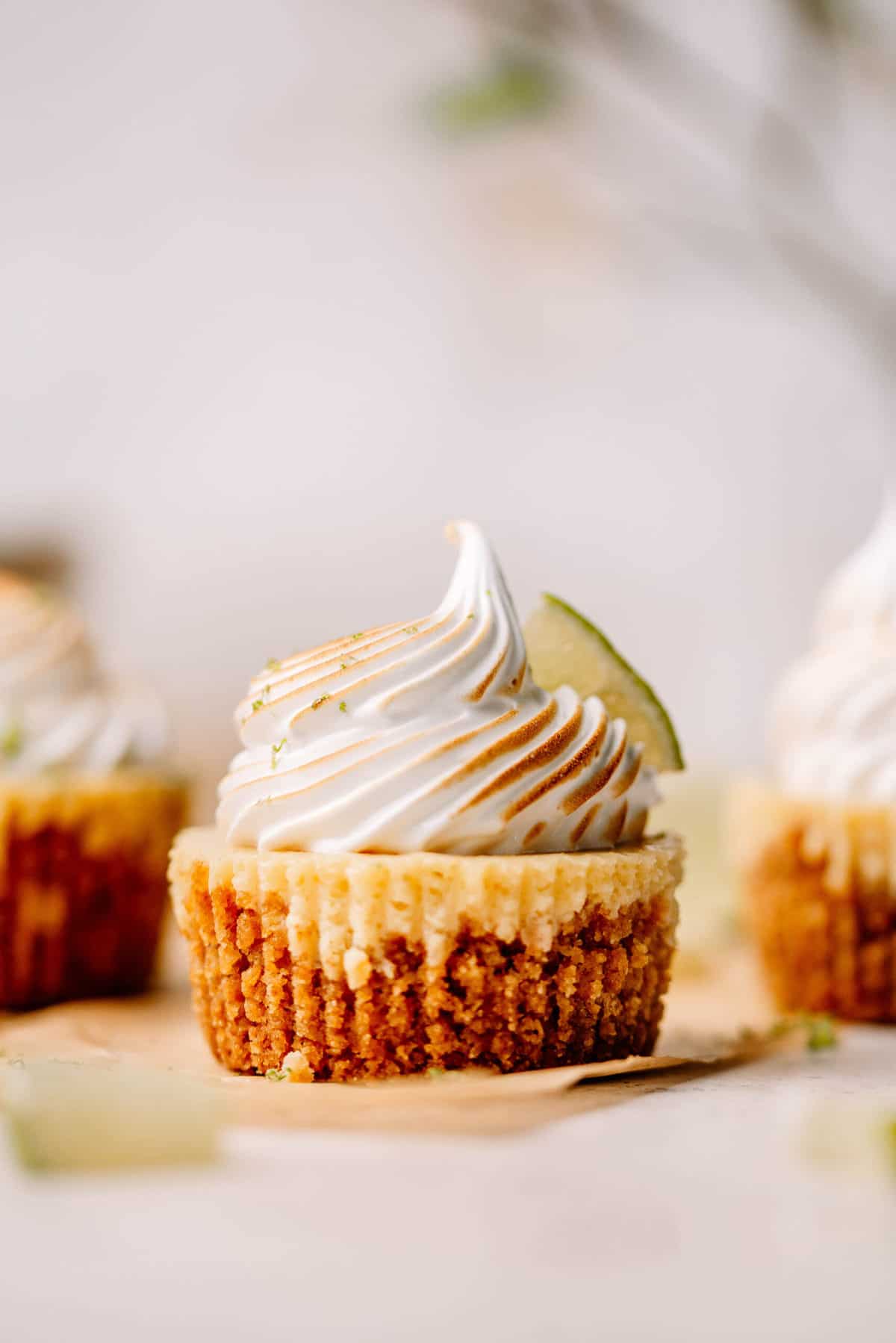 Mini key lime pie with meringue and a slice of lime on brown parchment paper.