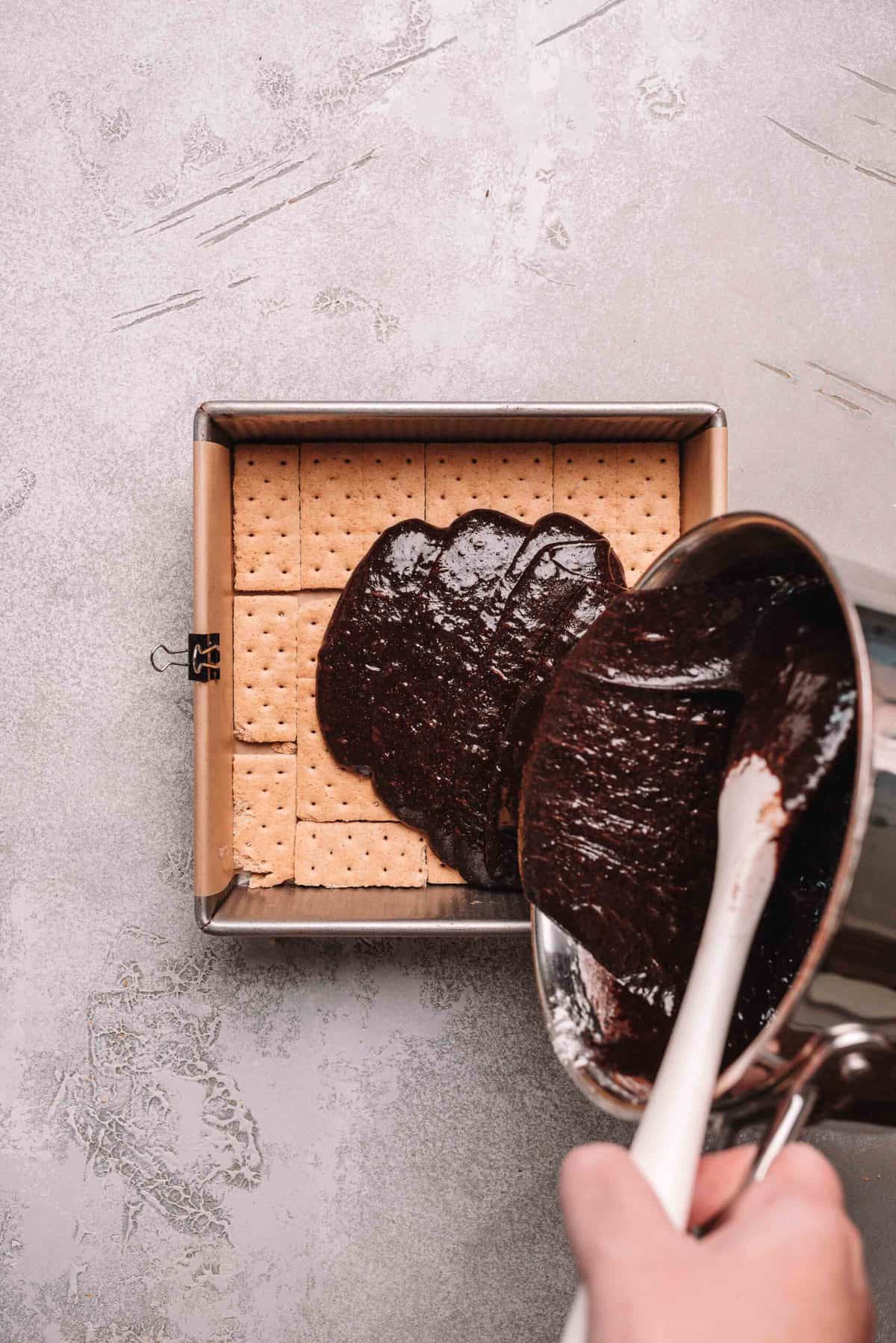 Brownie batter poured over graham crackers in a baking pan.