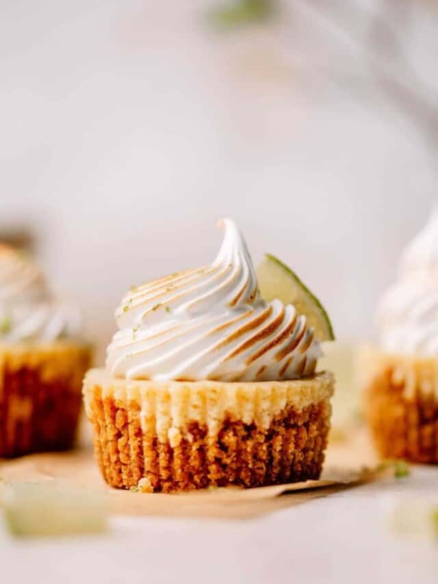 Mini key lime pie with meringue and a slice of lime on brown parchment paper.