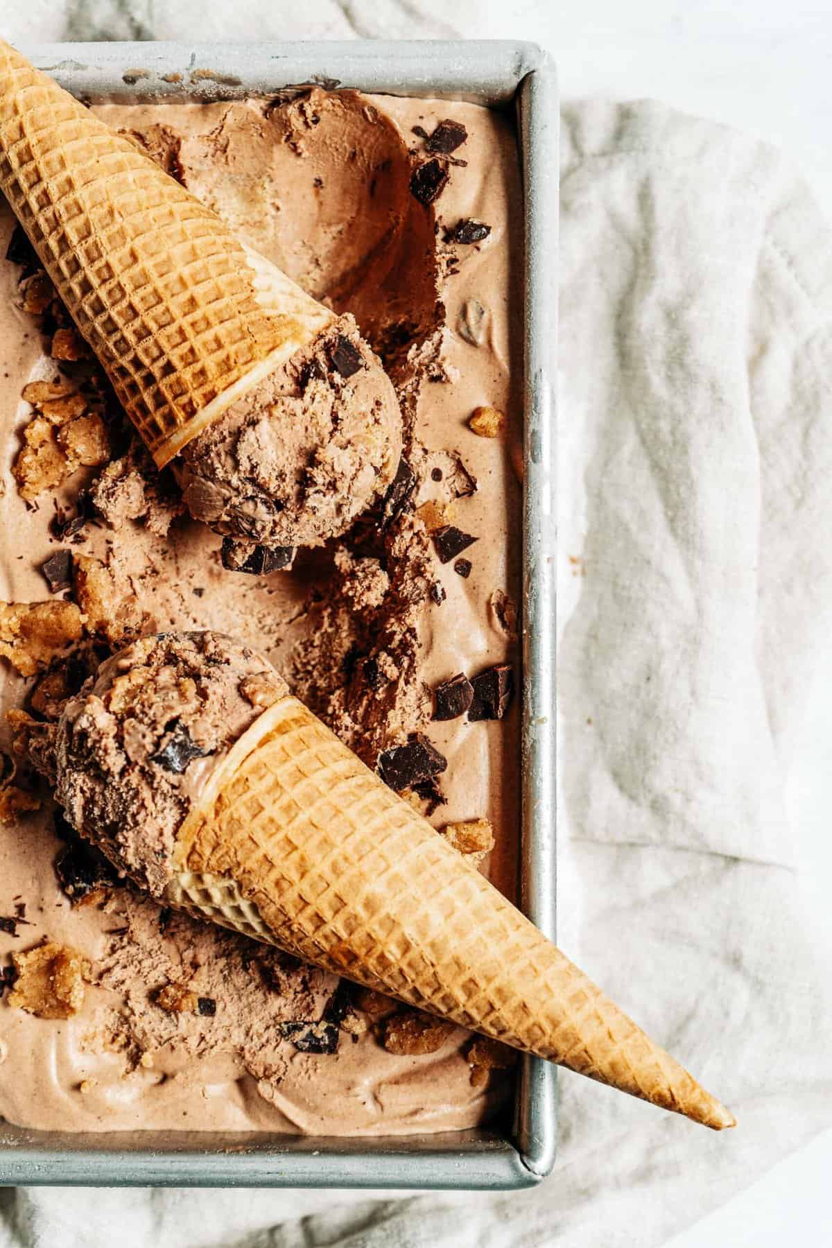 Chocolate peanut butter ice cream in a pan with two ice cream cones.