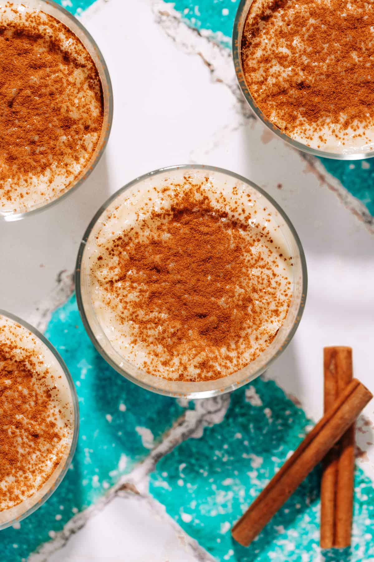 4 bowls of rice pudding topped with cinnamon and two cinnamon sticks.