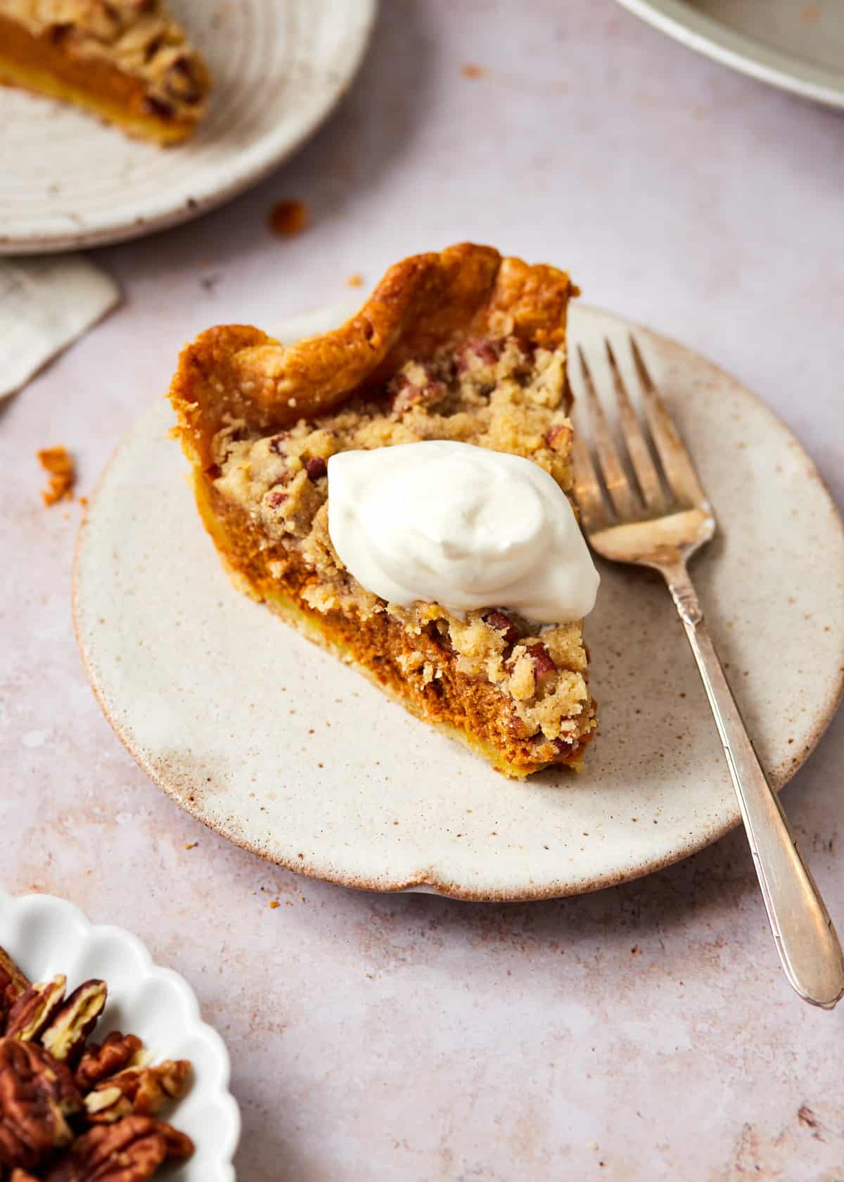 Slice of streusel pumpkin pie topped with whipped cream on a plate.