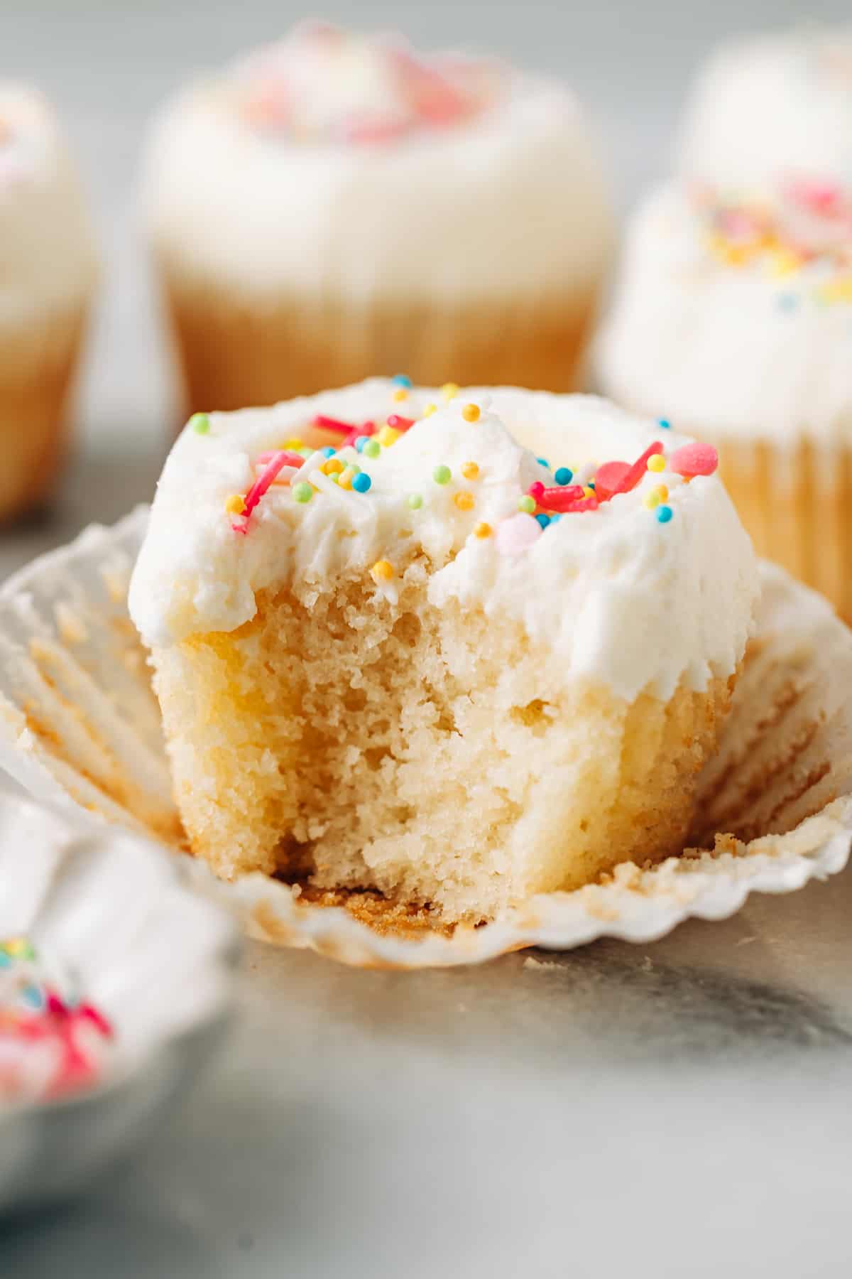 bite shot of a fluffy vanilla cupcake topped with buttercream frosting and sprinkles.